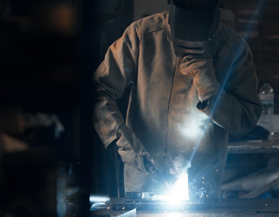 welder in protection mask working with metal at factory