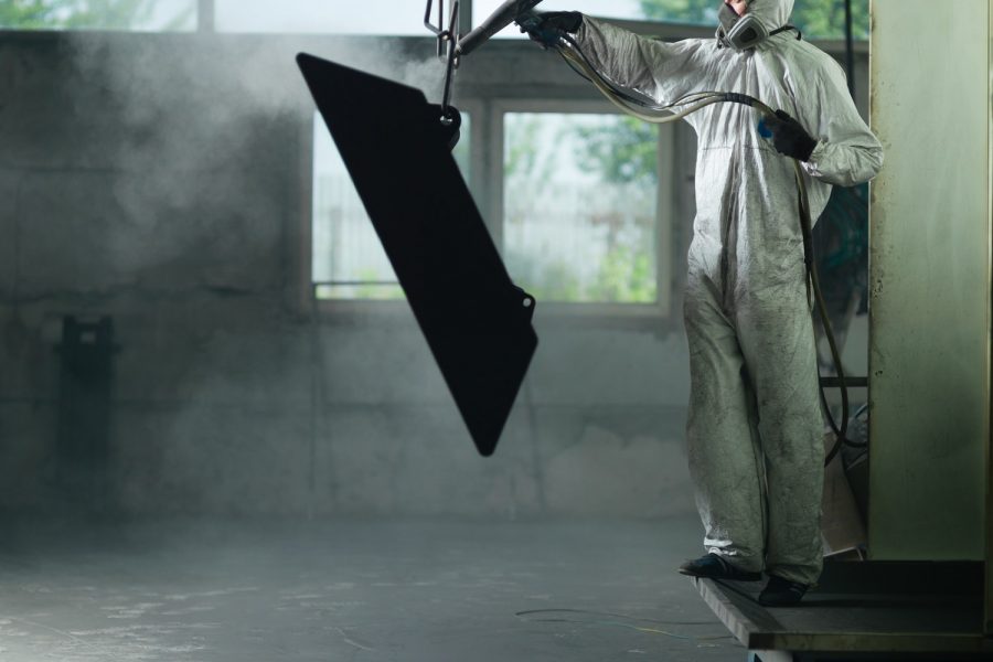 worker sand blasting a metal crate
